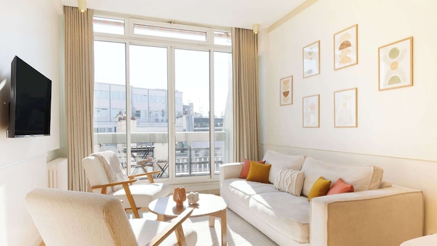 A modern living room with a sofa, armchair, and coffee table, large windows with curtains, and wall-mounted artwork. - A Luxurious 3BR/3BA with A/C in Opéra-Bourse (Paris)