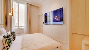 A hotel room with a large bed, a TV mounted on the wall, and a window with curtains. - An Elegant 1-BR/1Ba with Services in La Madeleine (Paris)