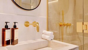 A modern bathroom with a marble sink, gold fixtures, and a glass shower enclosure. - An Elegant 1-BR/1Ba with Services in La Madeleine (Paris)