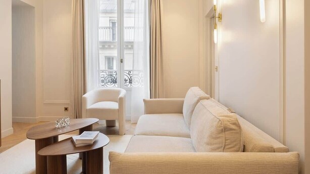 A modern living room with a beige sofa, a white armchair, and a wooden coffee table. - A Sophisticated 1-BR with Services in La Madeleine (Paris)