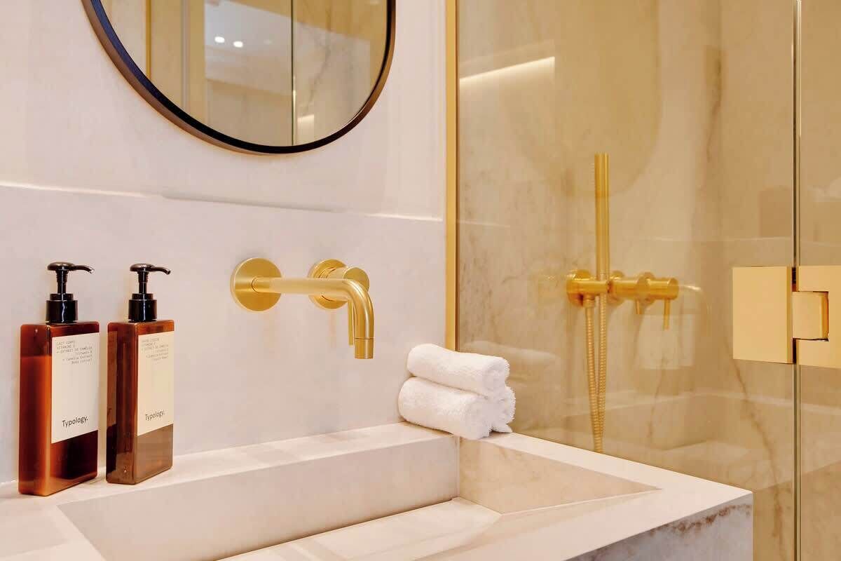 Ein modernes Badezimmer mit Marmorwaschbecken, goldenen Armaturen und einer Duschkabine aus Glas.