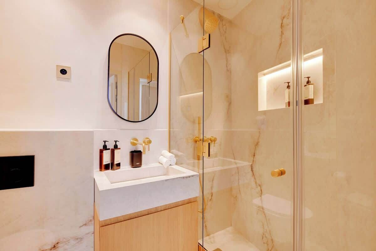 A modern bathroom with a marble vanity, a glass shower enclosure, and a large mirror.