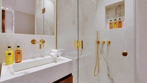 Ein modernes Badezimmer mit Marmorwaschtisch, goldenen Armaturen und einer integrierten Dusche.