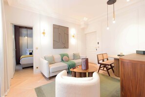 A modern living room with a sofa, a round coffee table, a white armchair, and a dining area with a wooden table and chairs. - A Romantic 1-BR with Services in La Madeleine (Paris)