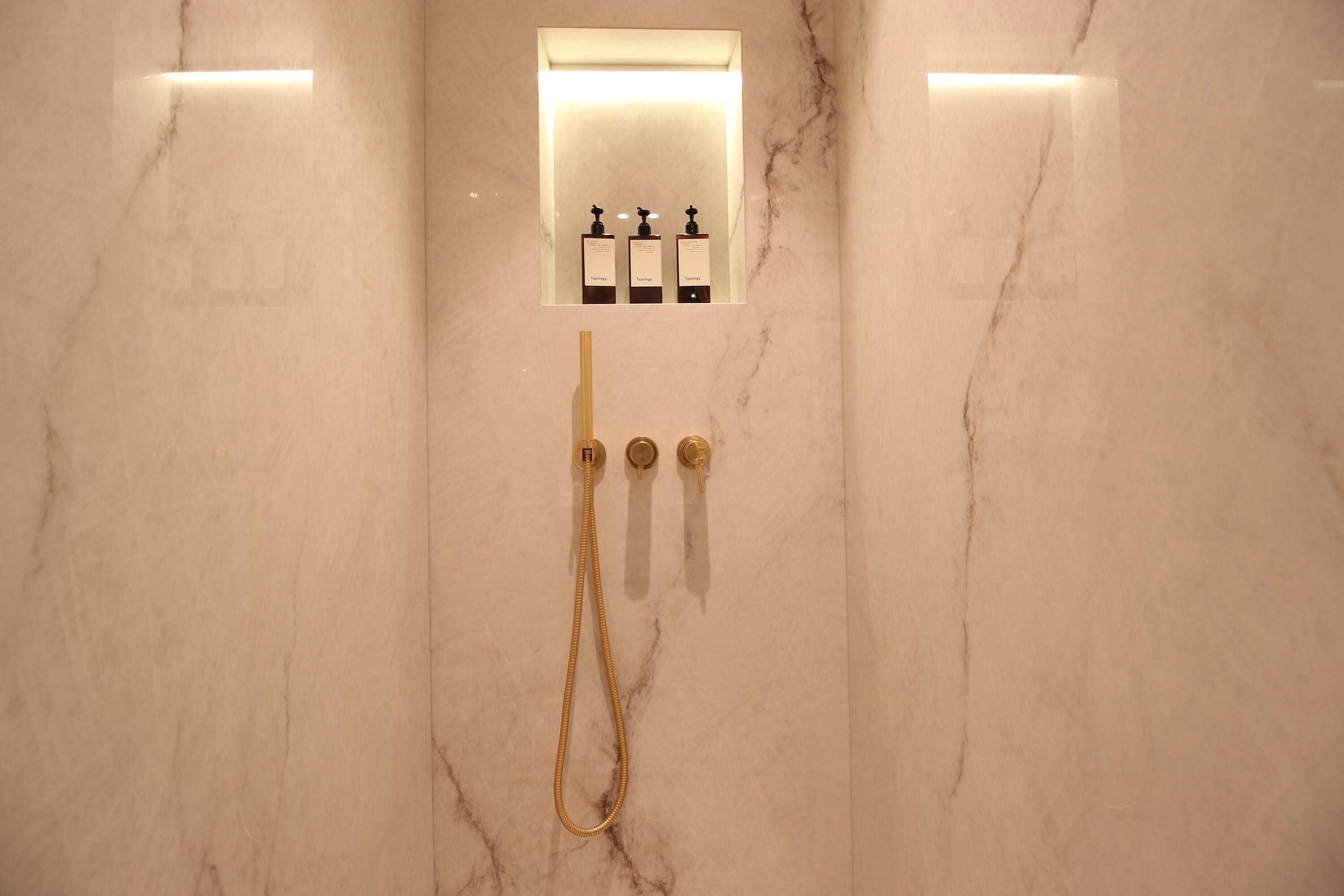Een marmeren wand met een douchebedieningspaneel en een handdouche.