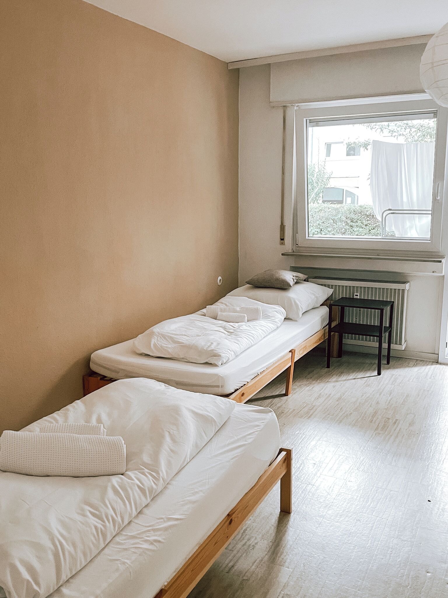 Una habitación pequeña y sencilla con dos camas individuales, una ventana con vistas y un radiador.