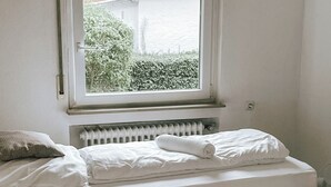 Ein Schlafzimmer mit einem Einzelbett, einem Fenster mit Blick auf Grünflächen und einem Heizkörper unter dem Fenster.