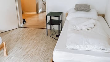 A bedroom with a wooden bed frame, white bedding, a small black nightstand, and a wooden chair.