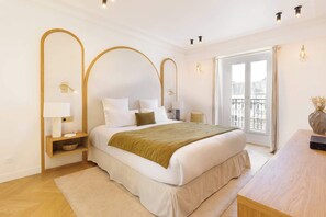 A modern bedroom with a large bed, bedside lamps, a wooden nightstand, a wooden desk, and a view of the outside. - A 5BR/4BA Duplex w/Services in La Madeleine-Opéra (Paris)
