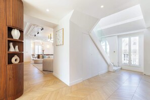 A spacious living area with a wooden cabinet, a staircase, and a large window. - A 5BR/4BA Duplex w/Services in La Madeleine-Opéra (Paris)