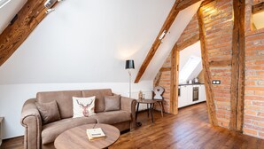 An attic-style room with exposed wooden beams, a brown leather sofa, a round wooden coffee table, and a brick wall. - "Suite Heimat" with King-Size Bed and Air Conditioning (Gengenbach)