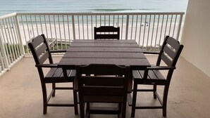 Een balkon met een houten tafel en stoelen, met uitzicht op een strand en de oceaan op de achtergrond.