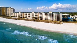 Een strandhotel met meerdere verdiepingen, een zandstrand en golven.