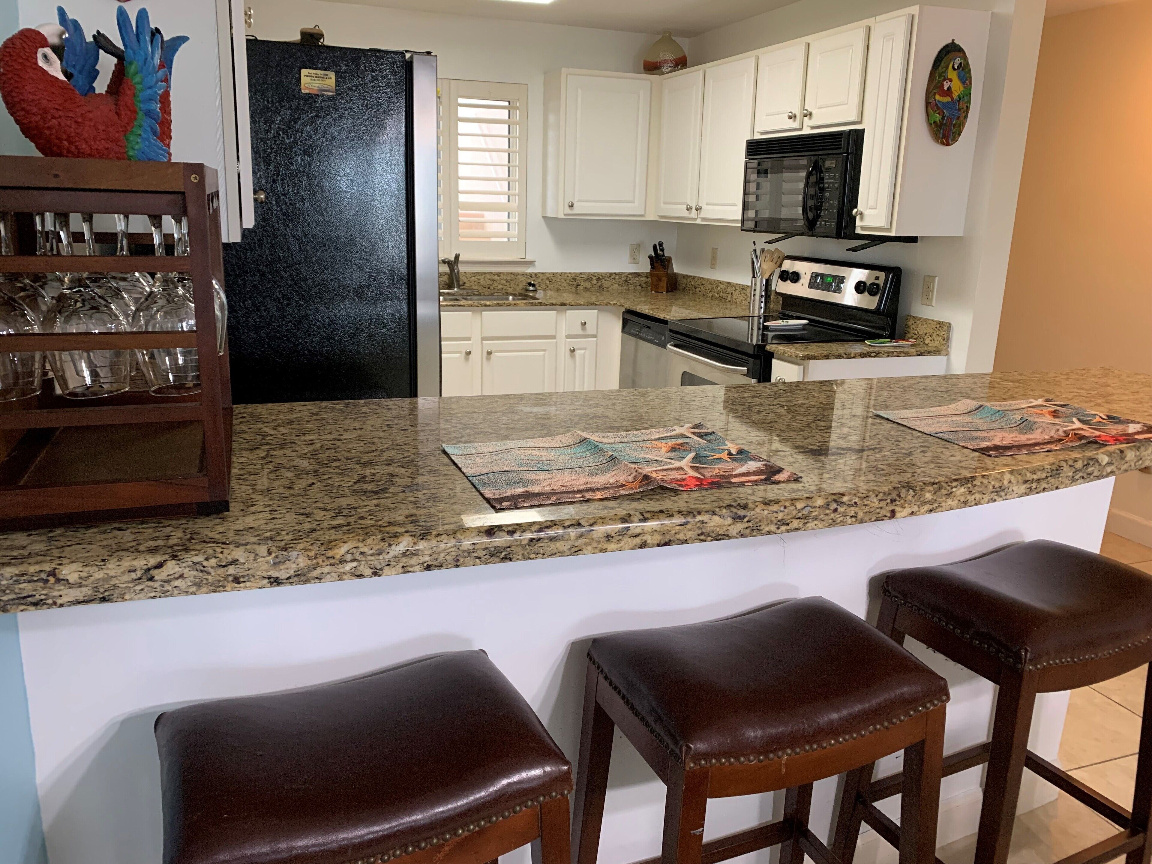 A kitchen with white cabinets, a black refrigerator, a microwave, and a stove. There are two bar stools and a glassware rack.