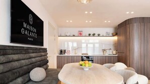 A modern kitchen with a central island, a dining area with a round table, and a sofa with cushions. - A Sophisticated 1-BR with Services - Louvre (Paris)