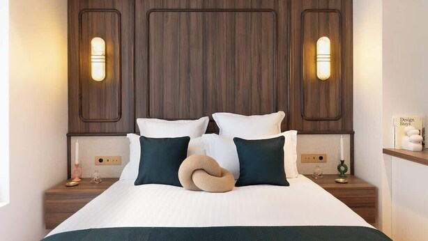 A hotel room with a large bed, two bedside tables, and a wooden headboard with built-in lighting. - A Sophisticated 1-BR with Services - Louvre (Paris)