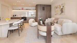 A modern living room with a sofa, a coffee table, and a dining area with chairs and a small table. - A Sophisticated 1-BR with Services - Louvre (Paris)