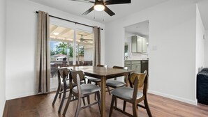 Un comedor con mesa y sillas de madera, un ventilador de techo y vista al patio trasero a través de una puerta corrediza de vidrio.