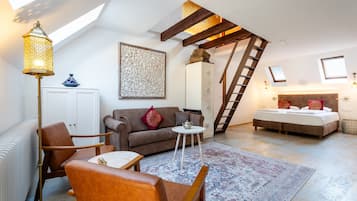 Ein Schlafzimmer im Loft-Stil mit schrägverdeckter Decke, einer Holzleiter, einem Bett, einer Couch, einem Couchtisch und einer Stehlampe.