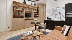 Una sala de estar moderna con sofá, mesa de centro y televisor. Hay una zona de cocina con estufa y alacenas.