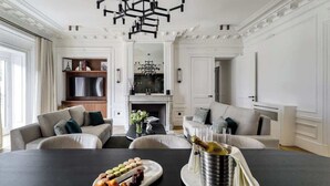 Un salon spacieux avec une cheminée, une table à manger dressée avec de la nourriture et des boissons, et un lustre moderne.