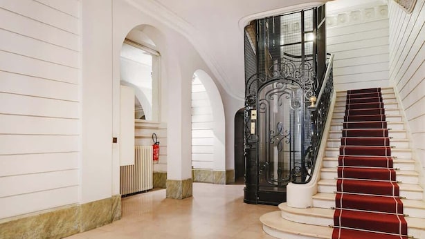 Un magnifique escalier, avec un tapis rouge, des murs blancs et une rampe noire richement décorée.