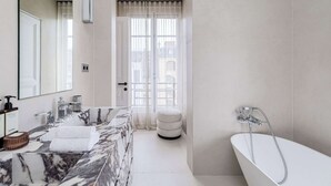A modern bathroom with a marble sink, a freestanding bathtub, and a large mirror. - ONIRI - Serviced 1-BR - Place Vendôme Louvre III (Paris)
