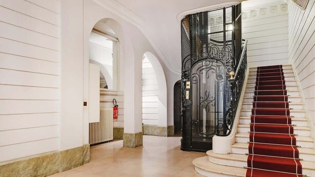 A grand staircase with a red carpet, white walls, and a black ornate railing. - ONIRI - Serviced 1-BR - Place Vendôme Louvre III (Paris)