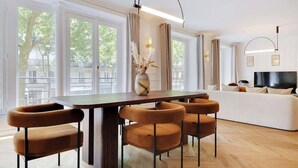 A modern living room with a dining area, large windows, and a flat-screen TV. - ONIRI - Somptuous Serviced 3-BR - Saint-Germain (Paris)