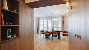 A modern dining area with a wooden herringbone floor, a central table with chairs, and a large window with curtains. - ONIRI - Somptuous Serviced 3-BR - Saint-Germain (Paris)