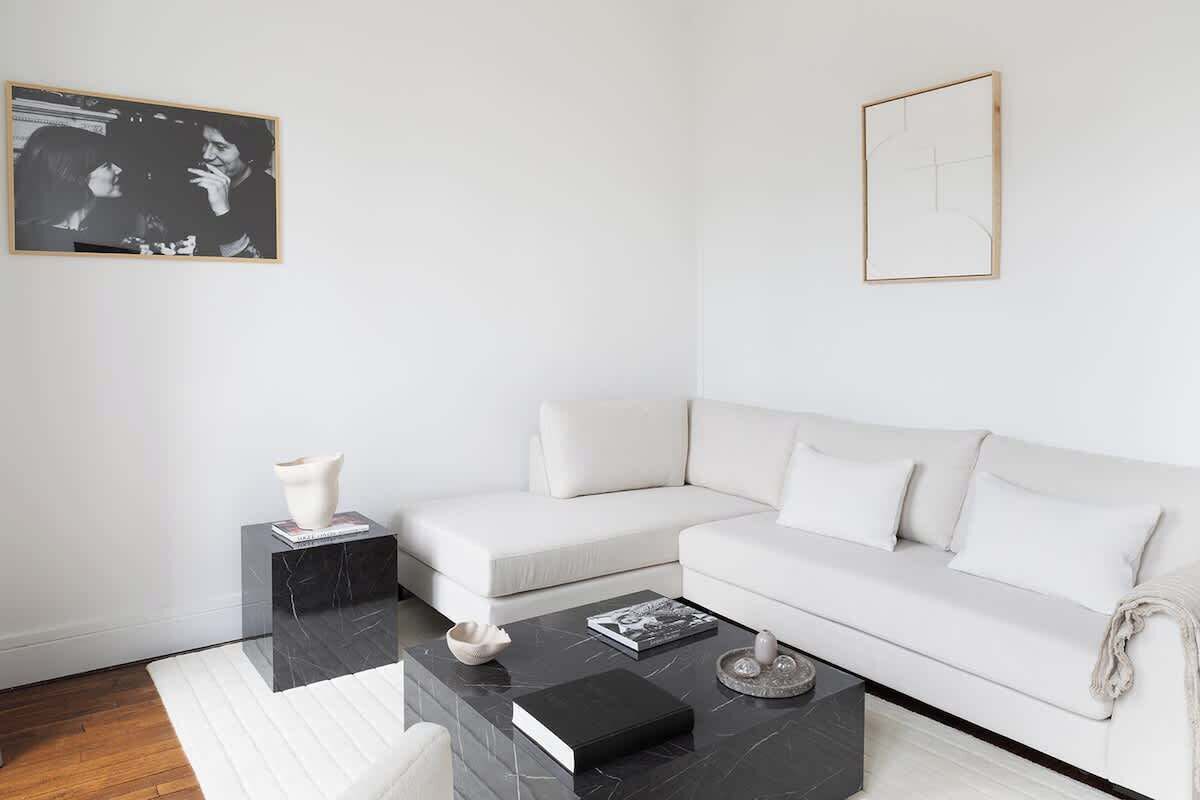 Un salon moderne avec un canapé d’angle blanc, une table basse en marbre noir et un tableau encadré accroché au mur.