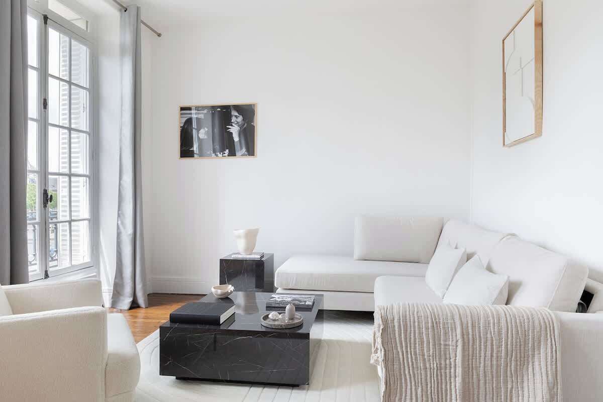 Un salon moderne avec un canapé blanc, une table basse noire et une œuvre d’art encadrée accrochée au mur.