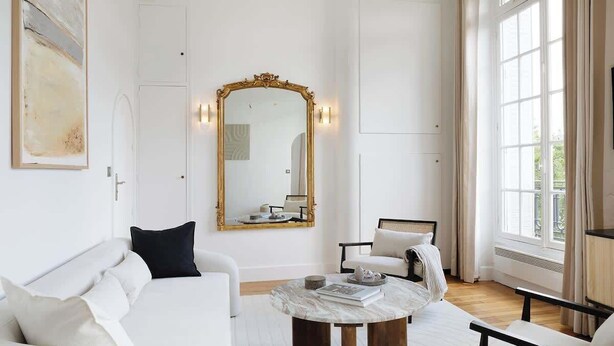 A spacious living room with a white sofa, a round coffee table, and a large mirror with a gold frame. - An Exceptional 1-BR au Quai des Orfèvres (Paris)