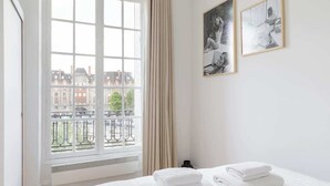 A hotel room with a large window, a bed with neatly folded white towels, and two black-and-white photographs on the wall. - An Exceptional 1-BR au Quai des Orfèvres (Paris)