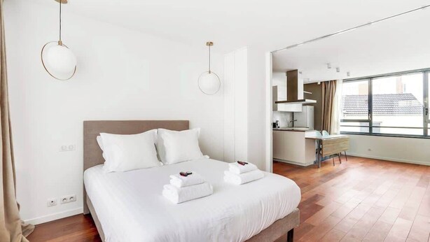 Quarto de hotel moderno com uma cama grande, uma escrivaninha e vista da cidade através de amplas janelas.