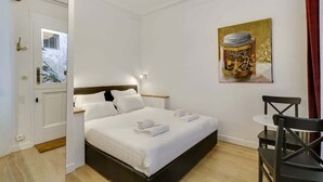 A neatly made bed with white linens and towels, a small table with a chair, and a painting on the wall. - A Sweet Studio in Montparnasse (Paris)
