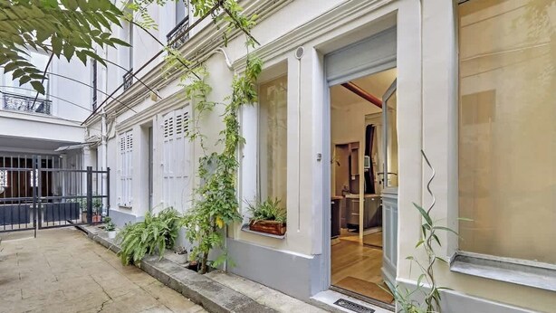 A building with a white facade, a visible entrance, and a small balcony with plants. - A Sweet Studio in Montparnasse (Paris)