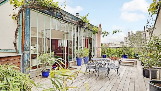 A wooden deck with outdoor furniture, potted plants, and a glass-enclosed area with a view of the city.