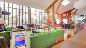 A spacious living area with large windows, a dining table, and colorful furniture.
