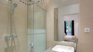 Un baño moderno con cabina de ducha de vidrio, un lavabo blanco y un espejo.