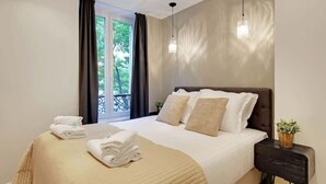 Habitación de hotel con cama, mesita de noche, planta en maceta y ventana con cortinas.