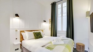 Un lit bien fait, avec un oreiller vert, une table de chevet avec une lampe et une fenêtre avec des rideaux.