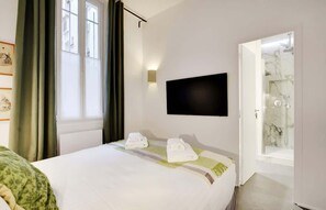 Quarto de hotel com cama, televisão fixada na parede e banheiro visível por uma porta aberta.