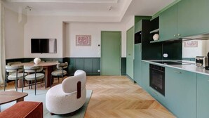 A modern kitchen with green cabinets, a dining area with a round table and chairs, and a cozy seating area with a white chair. - A Majestic 2-BR/2Ba w/ Services in Opera-St-Lazare (Paris)