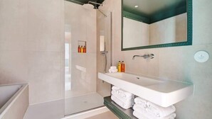 A modern bathroom with a glass shower enclosure, a white sink with a mirror above it, and neatly stacked towels. - A Majestic 2-BR/2Ba w/ Services in Opera-St-Lazare (Paris)