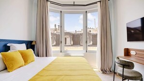 A hotel room with a large bed, a desk with a chair, and a view of the city through a large window. - A Majestic 2-BR/2Ba w/ Services in Opera-St-Lazare (Paris)