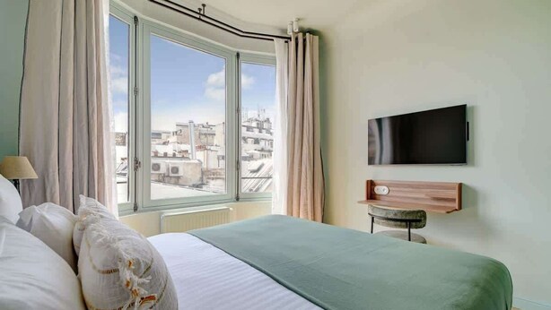 Ein Hotelzimmer mit einem großen Bett, einem an der Wand befestigten Fernseher und Blick auf die Stadt durch das Fenster.