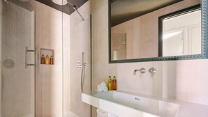 Ein modernes Badezimmer mit Glasdusche, großem Spiegel und Waschbecken mit Pflegeprodukten.