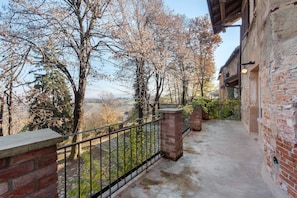 Un balcon avec un mur en briques, une rambarde en métal et une vue sur des arbres et un paysage lointain.