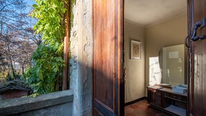 Een kamer met een houten deur, betegelde vloer, een spiegel en een raam met uitzicht op een tuin.
